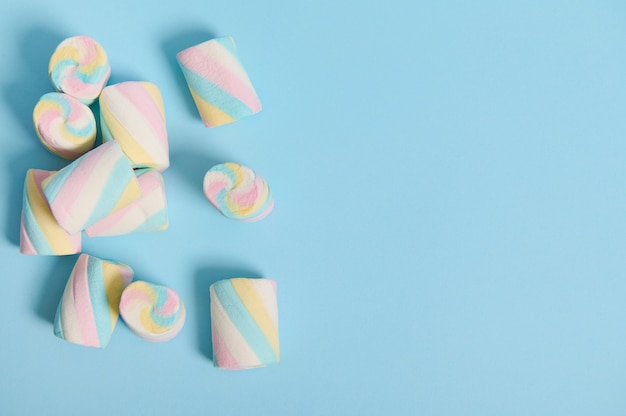 Photo flat lay minimalistic composition of colorful sweet marshmallows in the corner of a blue pastel background with copy space for advertising.