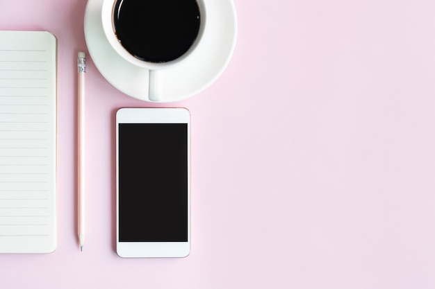 Flat lay of mobile phone, a cup of coffee and notebook of businesswoman on pink table in office. Business and technology concept top view and copy space.