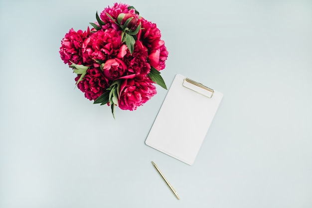 Flat lay mock up with clipboard and pink peony flowers bouquet on pastel blue surface