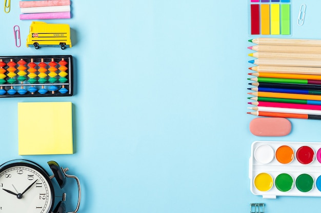 Flat lay of modern bright blue office desktop with school supplies on table around empty space for