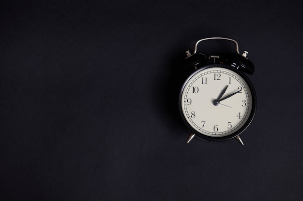 Flat lay monochrome composition with a vintage alarm clock on\
black background with copy space to add text. back to school and\
teachers day concepts, business, organization, time management,\
events