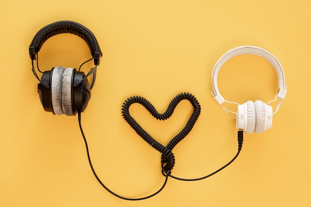 Photo flat lay musical composition with black and white headphones connected by a heart on a yellow background.