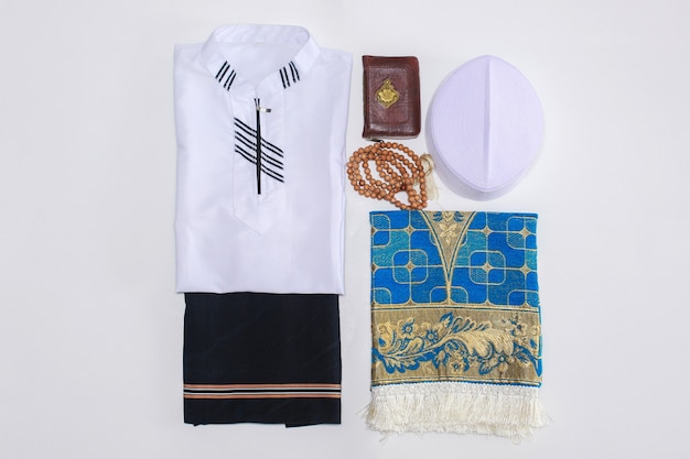 Flat lay of Muslim traditional dress and accessories for praying with Holy Book Al Quran and praying beads There is Arabic letter which means the holy book