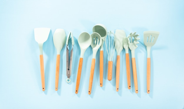 Flat lay. New blue silicone kitchen utensils with wooden handles on a blue background.