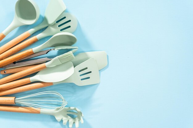 Flat lay. New blue silicone kitchen utensils with wooden handles on a blue background.