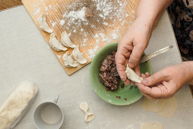 写真 年配の女性が生地からひき肉で餃子を準備する台所のテーブルのフラットレイ