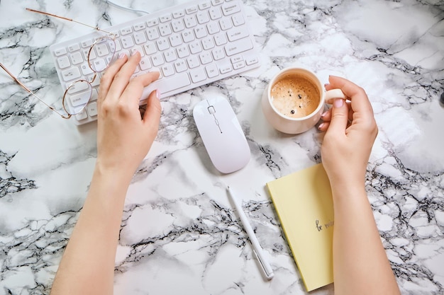 Flat lay office desk with Girl holds coffee Keyboard supplies cup of coffee on marble background Coffee break ideas notes goals or plan writing concept Top view