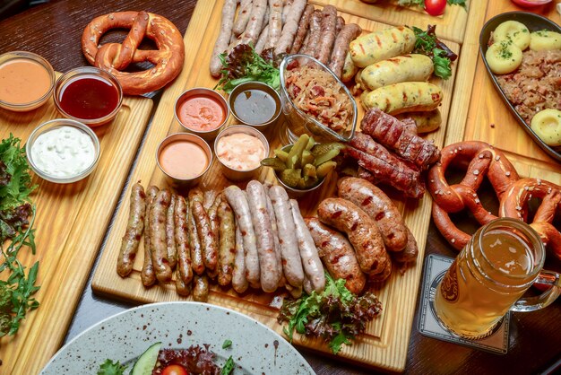 Piatto piano del tavolo da pranzo dell'oktoberfest con salsicce di carne alla griglia, pasticceria pretzel, patate, insalata di cetrioli, salse, birre