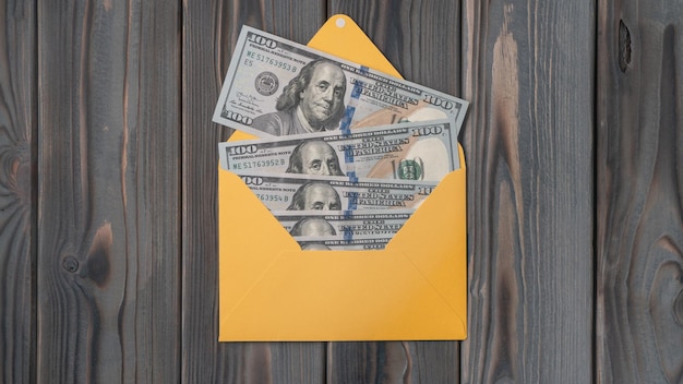 Flat lay of open yellow envelope with hundred dollars banknotes bills on wooden table Correspondence money salary