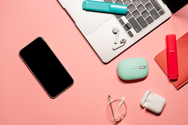 Flat lay on a pastel pink background with a silver laptop computer smartphone with a touch screen