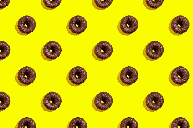 Flat lay pattern of tasty chocolate donut on yellow background