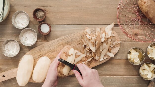 Flat lay. Peeling organic yellow potatoes with potato peeler.