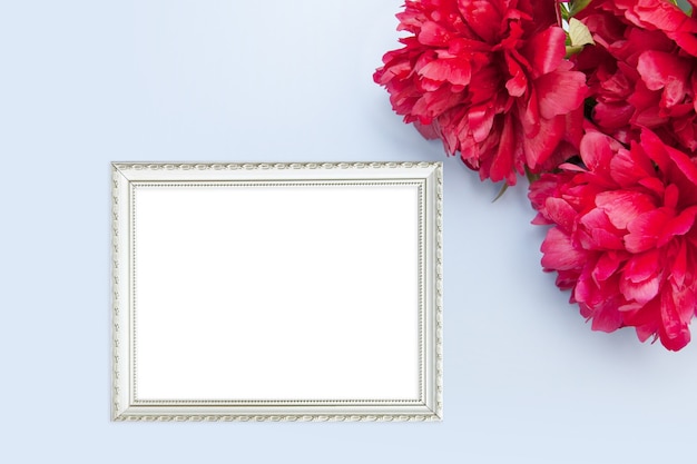 Flat lay photo frame mockup and peonies on a blue