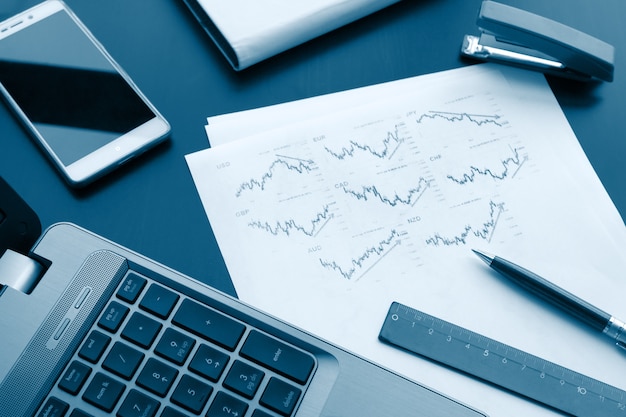 Flat lay photo of work desk with pen, laptop and chart paper