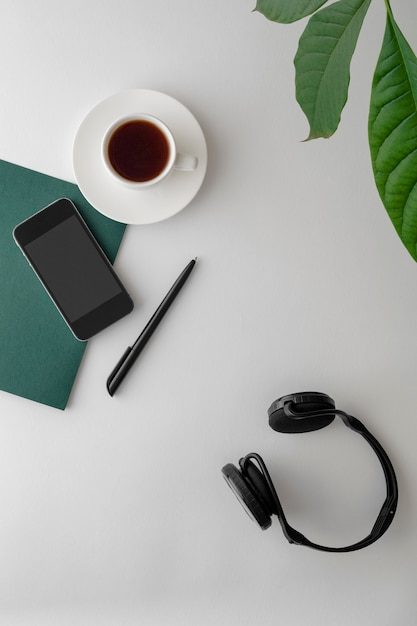 Flat lay photo of workspace desk with smartphone, earphones and green plant with copy space white surface