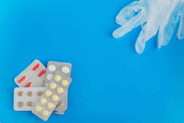 Flat lay of the pills blister packs and medical gloves  on the blue background with copyspace