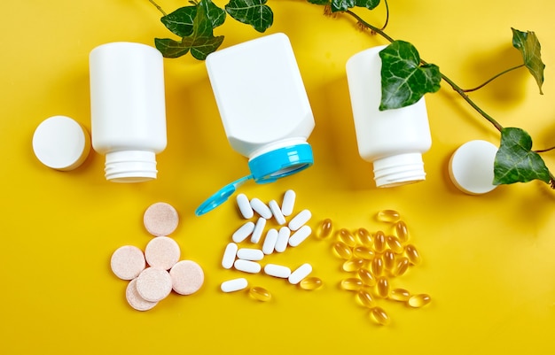Flat lay of pills, fish oil, vitamins  with green leaves on yellow