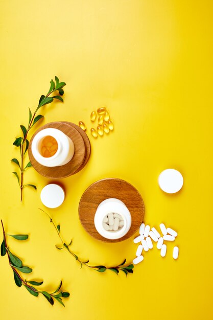 Photo flat lay of pills, fish oil, vitamins with green leaves on yellow