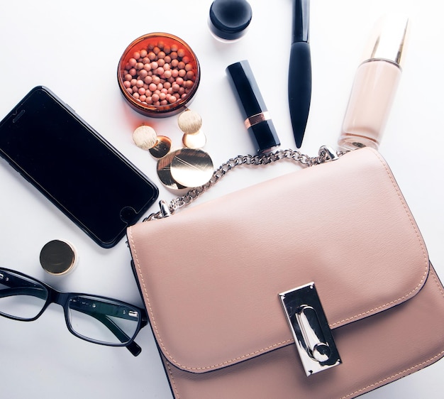 Flat lay of pink leather woman bag open out with cosmetics accessories and smartphone