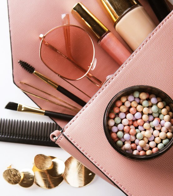 Flat lay of pink leather woman bag open out with cosmetics and accessories on white background