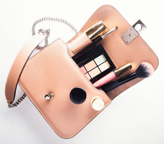 Flat lay of pink leather woman bag open out with cosmetics and accessories on white background