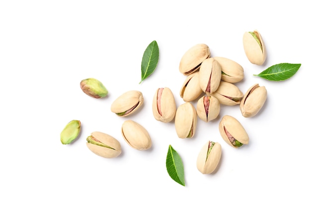 Flat lay of pistachio nuts with leaves on a white surface