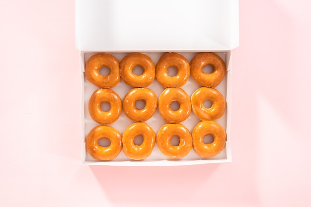 Плоская планировка. Обычные глазированные пончики, купленные в магазине, в белой бумажной коробке.