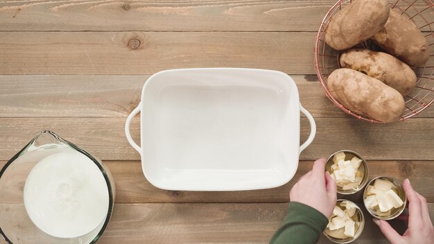 Flat lay. Preparing scalloped potatoes in a white ceramic baking dish.