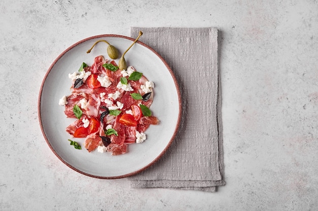 Flat lay prosciutto coppa di parma ham slices with ricotta cheese tomato capers and basil on light