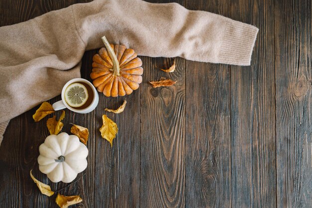 Flat lay of pumpkins dried leaves accessories and tea with lemon in cup on wooden background