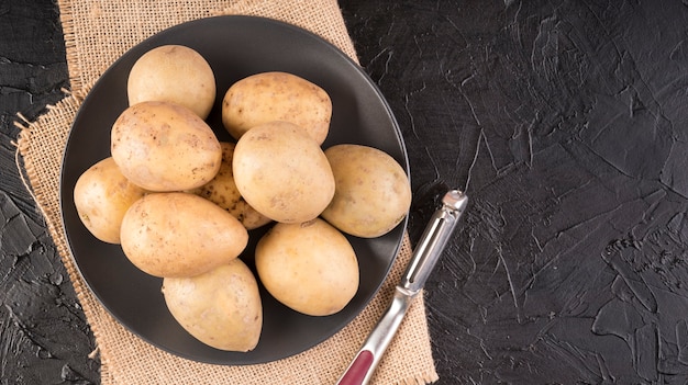 Photo flat lay raw potatoes on plate with copy space