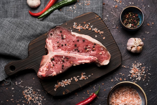 Flat lay raw t-bone steak with pepper and salt