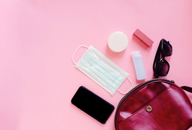 Flat lay of red leather woman bag open out with cosmetics, accessories, smartphone and mask