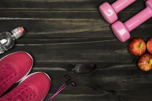 Flat lay of red sport shoes, dumbbells, earphones, bottle of water and apples on wood