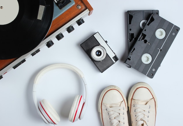 Flat lay retro 80s pop culture objects. Vinyl player, headphones, video tapes, film camera, sneakers on white background. Top view