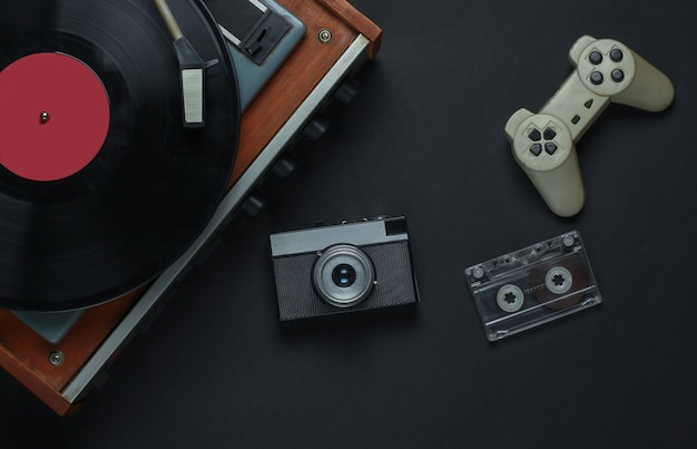 Photo flat lay retro media and entertainment. vinyl record player with vinyl record, film camera, audio cassette, gamepad on a black background. 80s. top view