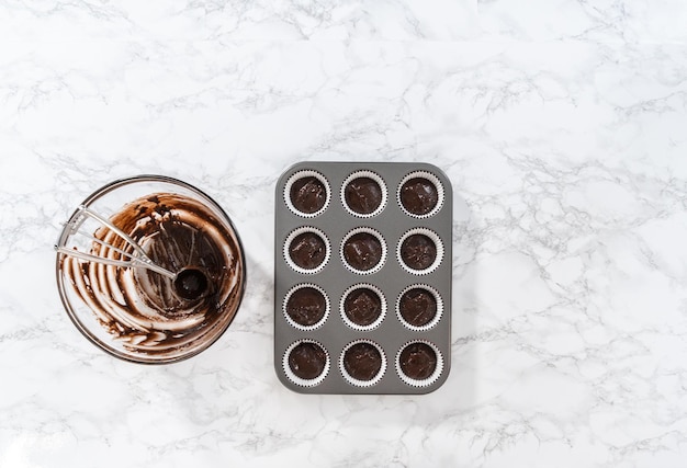 Flat lay. Scooping cake batter with dough scoop into cupcake foil liners to bake chocolate peppermint cupcakes.