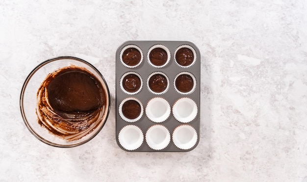 Flat lay. Scooping cupcake batter into the cupcake liners to bake chocolate strawberry cupcakes.