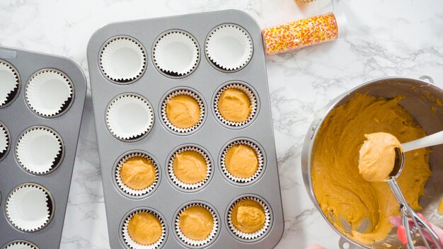 Foto disposizione piatta. versare la pastella per cupcake alle spezie di zucca con il cucchiaio per pastella in una teglia per cupcake con fodere.