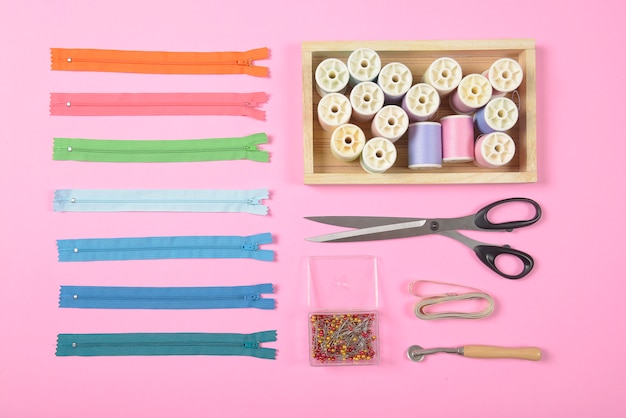 Flat lay of sewing material contains the scissors, measure tape, zipper and thread rolls.