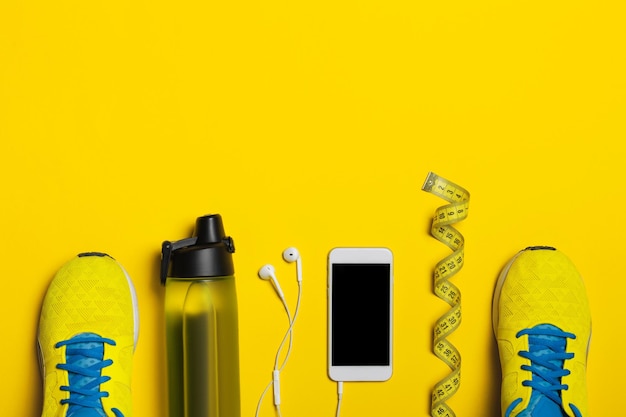 Плоский снимок спортивного инвентаря Кроссовки, водные наушники и телефон на желтом фоне