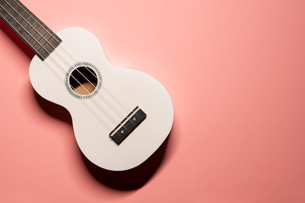 плоский снимок с милой маленькой белой гавайской гитарой укулеле с нейлоновыми струнами на пастельно-розовом