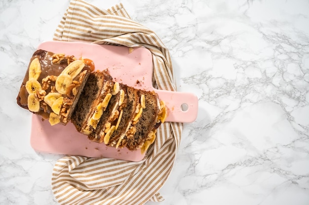 Flat lay. Sliced loaf of banana nut bread drizzled homemade caramel on a pink cutting board.