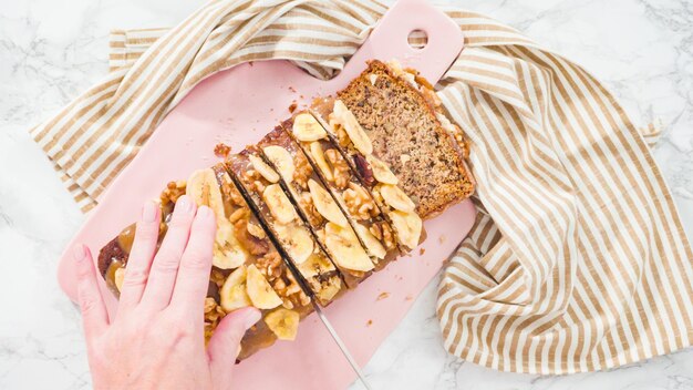 Flat lay. Slicing banana nut bread topped with caramel and garnished with banana chips and walnuts.