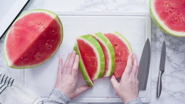 Flat lay. Slicing red watermelon into small pieces on a white cutting board.