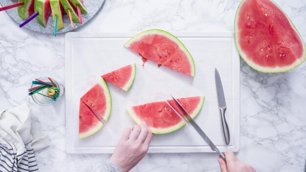 Flat lay. Slicing red watermelon into small pieces on a white cutting board.