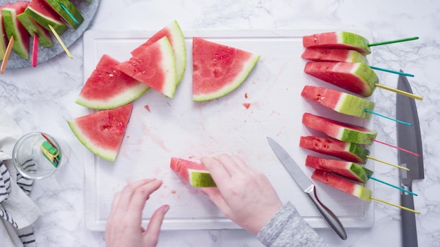 Flat lay. Slicing red watermelon into small pieces on a white cutting board.