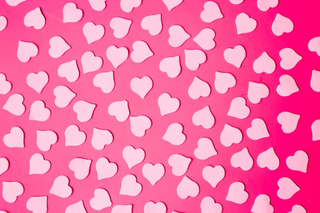 Flat lay of small hearts on a bright pink colored background