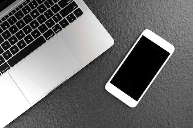 Flat lay of smartphone mock up with blank screen and laptop computer on black tabletop