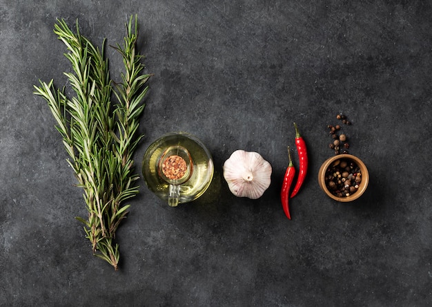 Flat  lay of  spices and fresh herbs rosemary garlic pepper chili pepper and oil on a dark gray background The concept of delicious and healthy food Top view and copy space